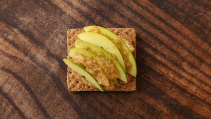 Whole grain cracker sandwich topped with peanut butter and fresh green apple slices on a wooden surface, overhead shot