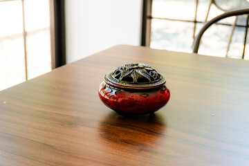Elegant red ceramic incense burner with a detailed brass lid on a warm, polished wooden table. Perfect for relaxation, meditation, and decor