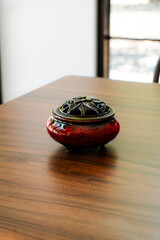Elegant red ceramic incense burner with a detailed brass lid on a warm, polished wooden table. Perfect for relaxation, meditation, and decor