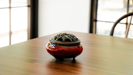 Elegant red ceramic incense burner with a detailed brass lid on a warm, polished wooden table. Perfect for relaxation, meditation, and decor