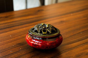 Elegant red ceramic incense burner with a detailed brass lid on a warm, polished wooden table. Perfect for relaxation, meditation, and decor