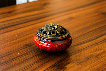 Elegant red ceramic incense burner with a detailed brass lid on a warm, polished wooden table. Perfect for relaxation, meditation, and decor