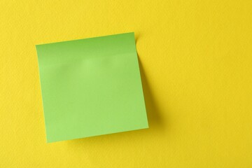 Blank green note on yellow background, top view. Space for text