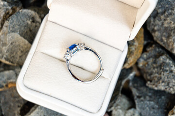 Stunning blue sapphire and diamond engagement ring in a white velvet box, perfectly set against a backdrop of natural grey rocks
