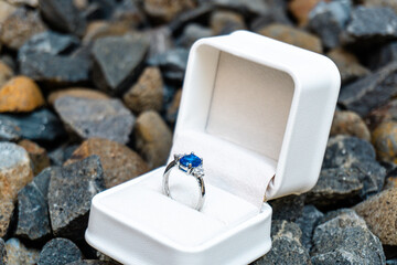 Stunning blue sapphire engagement ring in a white box, set against a backdrop of natural stones. Perfect for luxury and romance themes