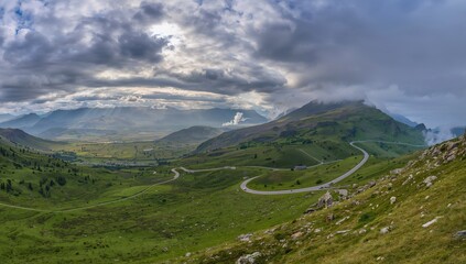 Naklejka premium Mountain highway winding through rugged terrain under cloudy skies