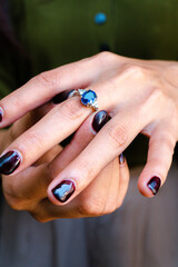 Close-up of a woman's hand wearing an elegant sapphire and diamond ring, with nails painted in a deep, rich burgundy color