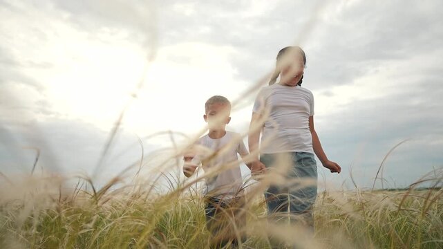 Girl and boy holding hands walking in field. Children running across grass together. Kid runs with sibling. Child enjoys moment. Hands together while running. Girl and boy smiling while running.