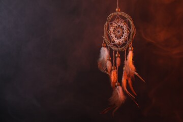 Beautiful dream catcher hanging in color lights against dark background with smoke, space for text