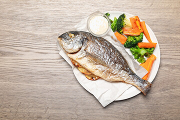 Tasty grilled fish, vegetables and sauce on wooden table, top view. Space for text