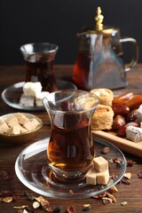 Traditional Turkish tea, brown sugar and sweets on wooden table, closeup