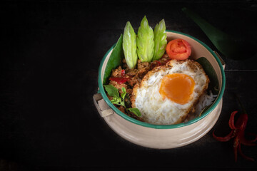 Beautifully presented stir-fried pork with basil and a fried egg, served in a vintage style plate garnished with fresh chilies, cucumber and herbs.