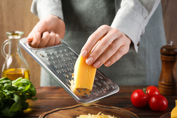 Woman grating cheese at wooden table, closeup