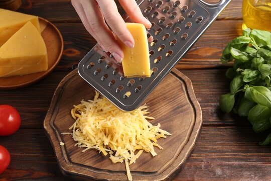 Woman grating cheese at wooden table, closeup - Powered by Adobe