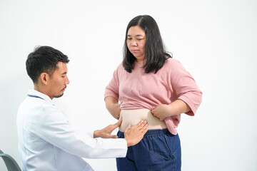 In a clinic, an Asian doctor in a white coat examines an obese Asian woman's abdomen for accumulated fat, notes on a clipboard, and offers advice on obesity and potbelly issues.