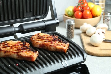 Electric grill with delicious steaks on light table in kitchen, closeup