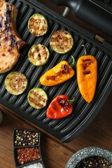 Electric grill with steak and vegetables on wooden table in kitchen, flat lay