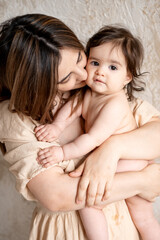 a mother with a baby, a young mom gently hugs and kisses her newborn baby, holding him in her arms, maternal love and care, a mother having fun with her child at home