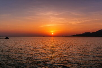 Obraz premium Beautiful sunset casting reflections on the water with a boat's outline