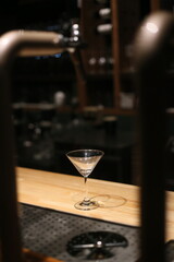 A solitary martini glass elegantly displayed on a polished wooden counter in a dimly lit bar setting