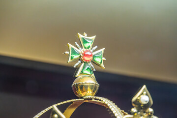 Close-up view of vibrant gemstone cross pendant with gold accents Multiple colored stones green, red, yellow in gold bezels, pearl detail at top, possibly historical or sentimental value, attached