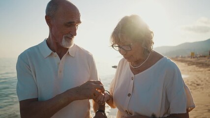 Happy senior couple walking hand in hand along the seashore at sunset, the woman showing the man a beautiful seashell she found, enjoying their retirement and creating romantic memories together - Powered by Adobe