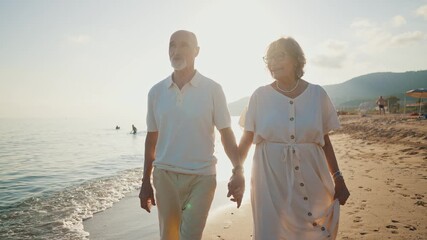 Happy senior couple walking hand in hand along the seashore at sunset, the woman showing the man a beautiful seashell she found, enjoying their retirement and creating romantic memories together - Powered by Adobe