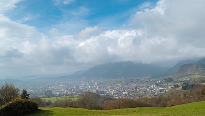 Naklejka premium Wide view of an urban area shrouded in mist with hills and a cloudy blue sky, seasonal transition, travel, nature, greenery, scenery, architecture, fall, elevation