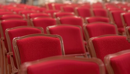 Rows of red velvet seats with wooden trim arranged inside a room. Close-up with selective focus.