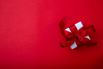 White luxury gift box with satin red ribbon on elegant red background. Sophisticated composition for jewelry and premium gift branding.