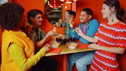Diverse group of young friends enjoying a meal together in a stylish and colorful restaurant. Cheerful people laughing, talking, and eating with chopsticks, creating a warm and lively atmosphere - Powered by Adobe