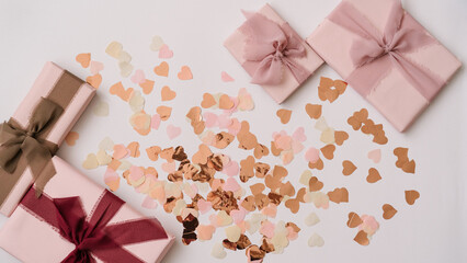 Flat lay composition with pastel gift boxes and heart-shaped confetti in pink, peach, and gold tones. Romantic celebration aesthetic.