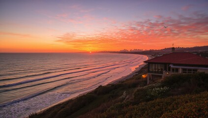 Coastal sunset over the ocean with waves, houses, and sky