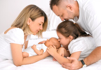 The older sister gently kisses her newborn brother. A baby surrounded by loving parents.
