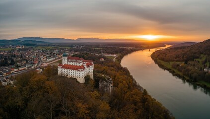 Bird's-eye view of a majestic hilltop fortress during a dramatic autumn sunset with a winding river and golden sky in the distance