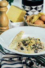 Delicious pasta with olives and herbs, with a slice of toasted bread, elegantly presented on a white plate.