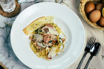 A plate of delicious spaghetti carbonara with a slice of garlic bread and some eggs