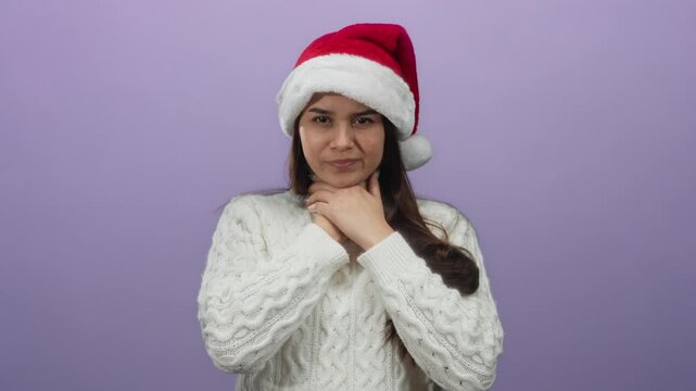 Woman in red santa hat holding throat in discomfort over isolated purple background reflects seasonal health concern during holidays.