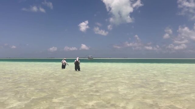 Two fly fishermen wade across the crystal-clear tropical flats of Kiritimati (Christmas Island), Kiribati, in search of bonefish. The expansive shallow lagoon, turquoise water, and distant horizon cre