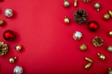 Red background with Christmas decorations on edges. Golden, red and white baubles, pinecones and nuts forming festive frame with copy space.