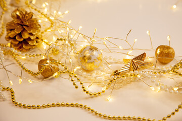 Fototapeta premium Christmas and New Year golden pinecone background with glowing garland and pearls. Cozy festive composition with copy space for text or design.