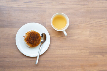 Top-down view of Ketan Serundeng (or Ketan Bintul), an Indonesian traditional sticky rice dish with toasted coconut, served on a white plate with a cup of tea on a wooden table.