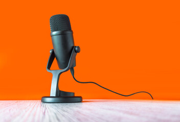 microphone on a wooden table with an orange background, symbolizing podcasting, broadcasting, or voice recording