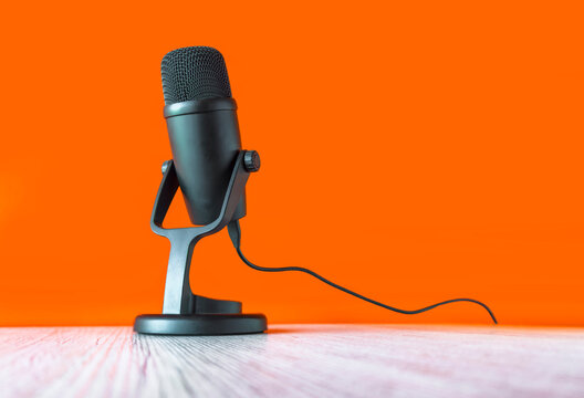 microphone on a wooden table with an orange background, symbolizing podcasting, broadcasting, or voice recording