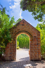 Charming brick archway with wrought iron gates opens to lush garden path under bright blue sky