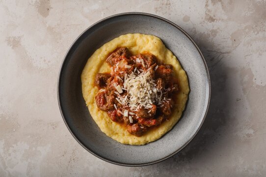 Contemporary take on classic Italian polenta alla sarda featuring sausage, minced meat sauce, and pecorino cheese presented from above in a ceramic dish