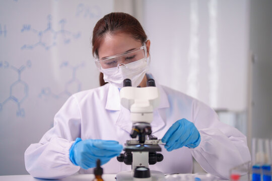 Asian adult woman scientist performs vital research observes samples microscope lab laboratory chemical formulas display experiment study