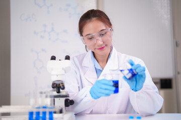 Asian adult female scientist conducting chemistry experiment pouring liquid beaker modern laboratory professional research science analysis