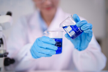 Adult Asian scientist pouring blue chemical liquid in science lab for scientific experiment research development
