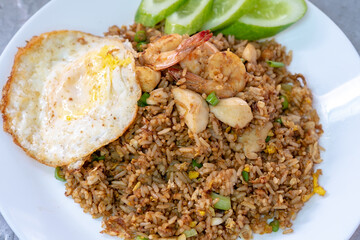 A plate of Indonesian nasi goreng, or fried rice, is served with shrimp, meatballs, a sunny-side-up fried egg, and slices of fresh cucumber.